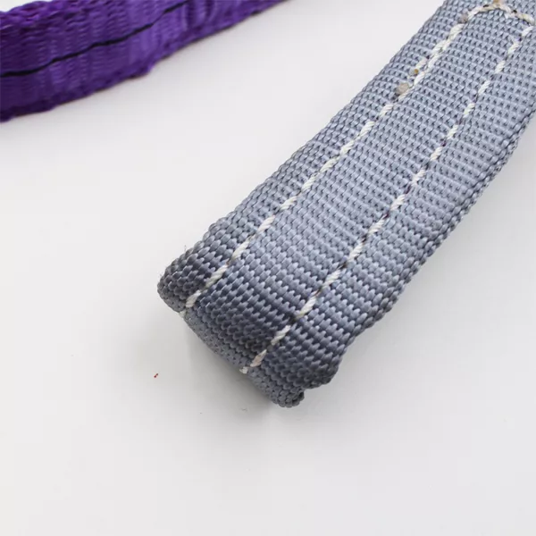 Close-up of a 1T Synthetic Webbing Sling with white background and a portion of a purple woven basket visible.