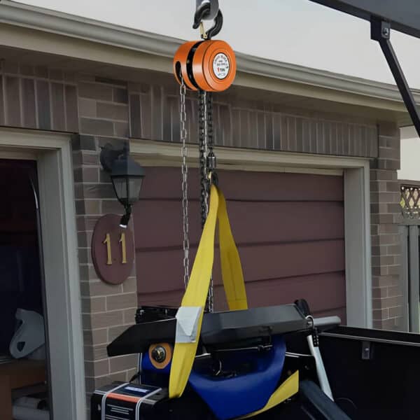 An orange chain hoist on a yellow strap lifts a heavy object near a brick building with door number 11.