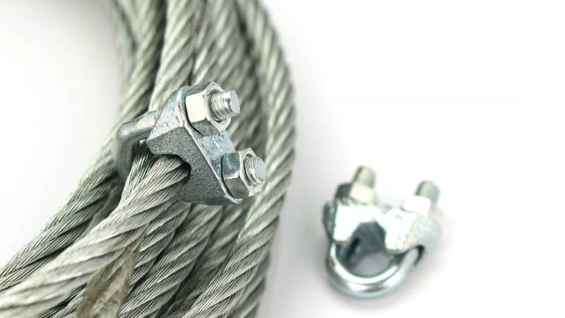 Close-up of a steel wire rope secured with a U-bolt clamp by top manufacturers, with another clamp nearby on a white surface.