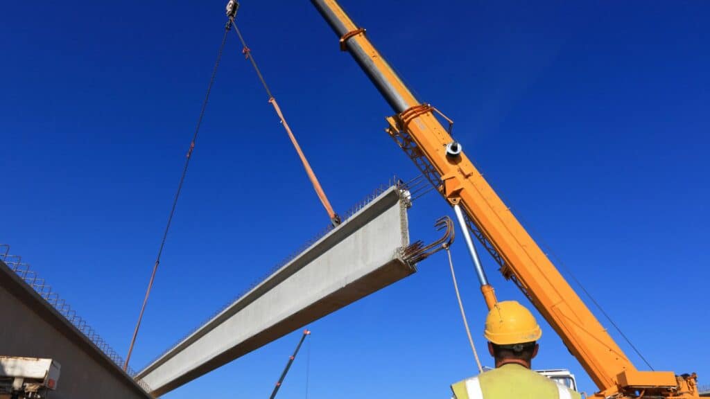 a crane lifting a steel beam with a wire rope hoist and a set of slings